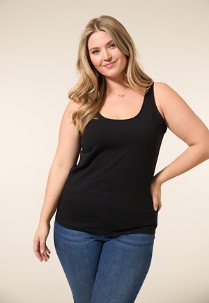 Zwarte mouwloze tanktop van zacht materiaal, met een ronde halslijn en een slim-fit ontwerp, gecombineerd met blauwe jeans.
