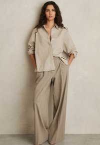 Beige button-up shirt met opgerolde mouwen, gecombineerd met beige gestreepte wijde broek. Gladde stof textuur, relaxte pasvorm.