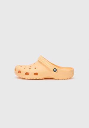 Orange plastic clog with a curved design, ventilation holes, and a strap. Features a black circular logo on the side and textured outsole.