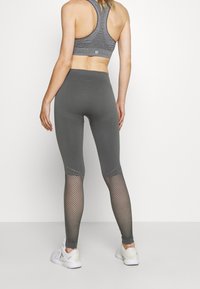 Szare legginsy sportowe z teksturowanym pasem w talii i siateczkowymi panelami na dolnej części nóg, w połączeniu z szara sportową biustonoszem i białymi sneakersami.