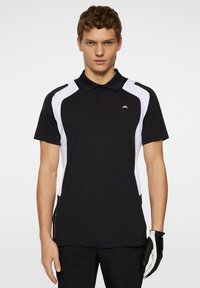 Svart och vit polo med krage, med sidopaneler i vitt, korta ärmar och en liten logotyp på bröstet.