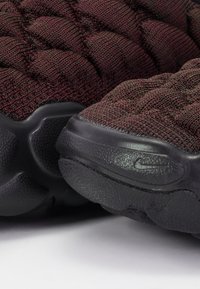 Athletic shoes featuring a dark maroon knitted upper with a quilted pattern, complemented by a textured black rubber sole.