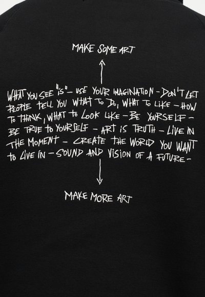 Άσπρο χειρόγραφο κείμενο σε μαύρο ύφασμα λέει: «Χρησιμοποίησε τη φαντασία σου, γίνε ο εαυτός σου, ζήσε τη στιγμή, δημιούργησε τον κόσμο που θέλεις. Δημιούργησε τέχνη. Δημιούργησε περισσότερη τέχνη.»