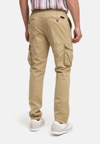 Pantalones cargo beige con múltiples bolsillos, tela suave, corte relajado y detalles de costura. Combinados con zapatillas blancas.