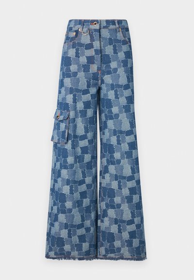 Široke traperice u plavom denimu s velikim patchwork uzorkom, strganim rubom i bočnom džepom s detaljem dugmeta.
