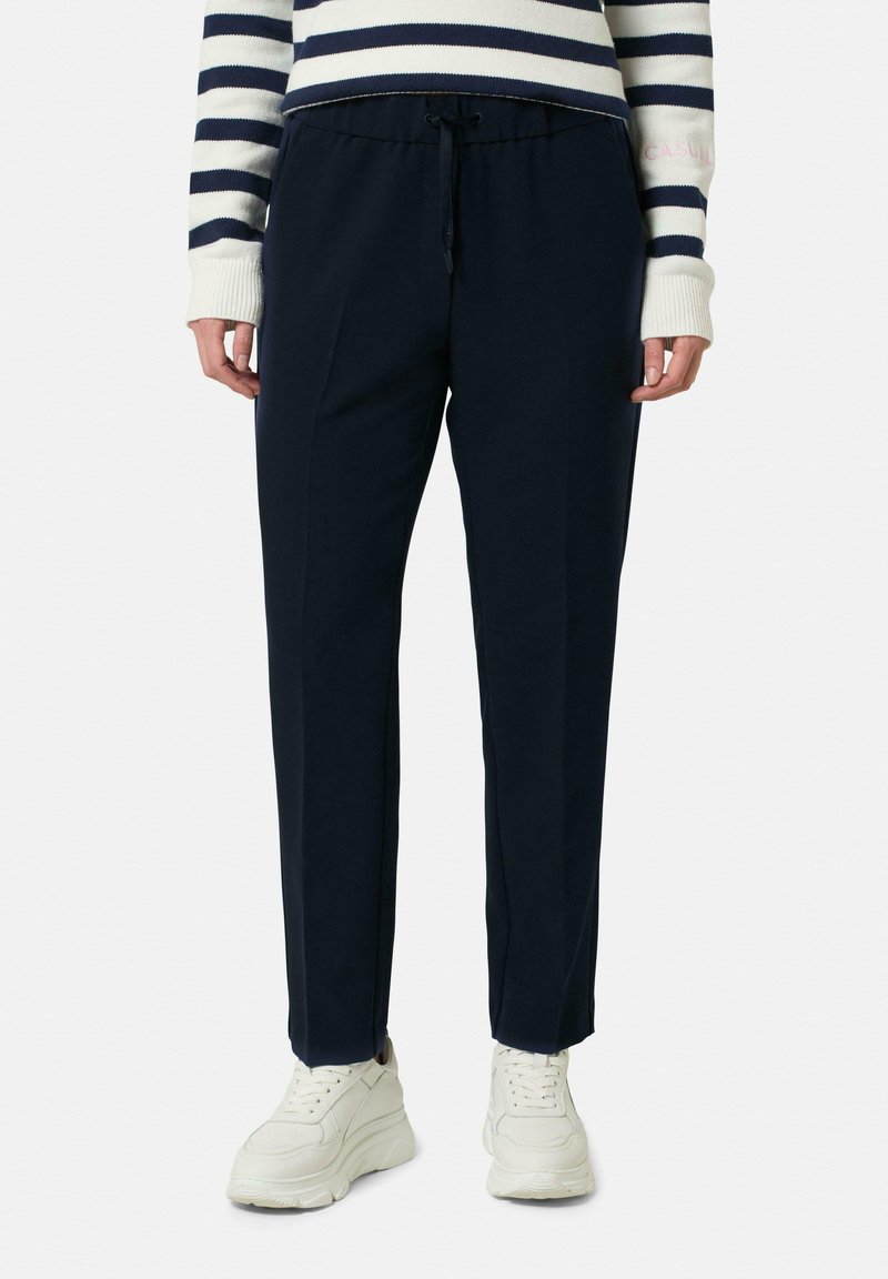 Marineblauwe trainingsbroek met een drawstring taille, taps toelopende benen en zijnaad. Gecombineerd met witte sneakers. Zachte, gladde stofstructuur.