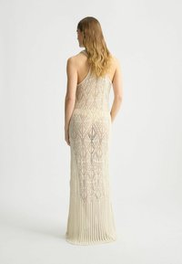 Vista posteriore di un vestito a maglia color crema caratterizzato da un motivo a diamante, corpetto aderente e parte inferiore plissettata, con scollo a halter.