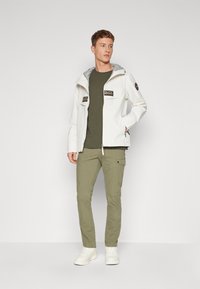Hvid vandtæt jakke med grå hætte, to forlommer, olivengrøn t-shirt, olivenfarvede cargo bukser og hvide sneakers.