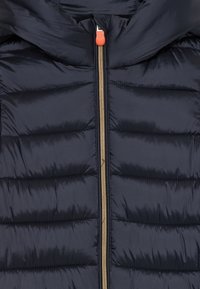 Marineblå quilted jakke med vertikalt guld lynlås og orange lynlås træk, der viser polstrede sektioner og kraveområde.