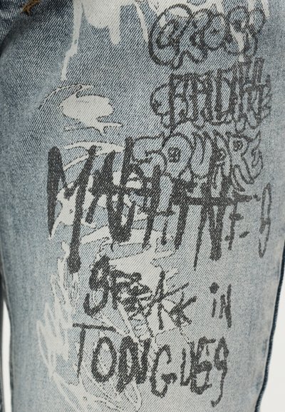 Denimpüksid helesinise pesuga, millel on musta graffiti-stiilis tekst ja mustrid, sirge säärega lõige ning nähtavad õmblused.