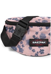 Ledvinka Eastpak z růžové látky s námořnicky modrým květinovým vzorem. Má černý nastavitelný popruh a značkovou nášivku. Zapínání na zip, hladká textura.