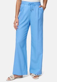 Light blue wide-leg pants with a drawstring waist, pleats, and pockets. Paired with white sandals featuring a cut-out design.