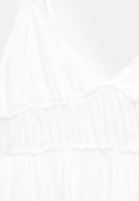 Tessuto bianco fluente con un design testurizzato e arricciato. Presenta spalline sottili e cuciture a strati per un tocco di dettaglio in più. Aspetto leggero e arioso.