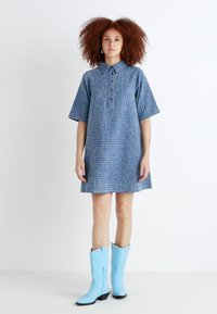 Robe à manches courtes bleue à motifs avec un col, dotée d'une fermeture à boutons sur le devant. Associée à des bottes de cowboy bleu clair.