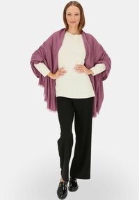 Przesadzony szal w kolorze śliwkowym z frędzlami zarzucony na białym swetrze o fakturze, w połączeniu z czarnymi spodniami dzwonami i błyszczącymi czarnymi butami.