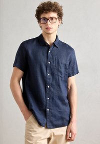 Marineblauw linnen overhemd met korte mouwen, met een zak, knoopsluiting en een ontspannen pasvorm. Soepele textuur, lichtgewicht stof.