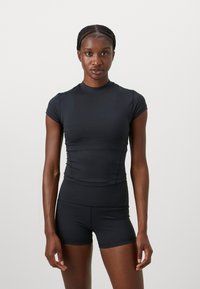 Haut de sport noir ajusté à manches courtes et col montant, associé à un short assorti. Tissu lisse et extensible, lignes épurées et design minimaliste.