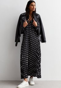 Black pleated maxi dress with white polka dots, layered under a black leather biker jacket. Paired with white sneakers.