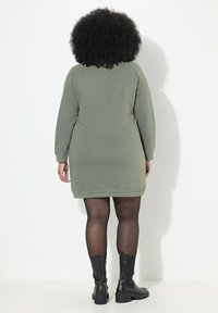Vestido sudadera de algodón verde con mangas largas y puños acanalados, que presenta una silueta recta y se lleva con botas altas negras.