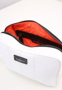 Vit texturerad läderpåse med svart dragkedja och orange inredning som har små svarta blixtm önster.