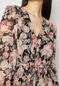 Vestido floral con fondo negro y patrones de rosas en tonos rosas y crema, con mangas largas de tela transparente, escote en V y detalle de cintura atada.