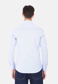 Camicia a strisce azzurro chiaro con maniche lunghe, polsini a bottone e un yoke posteriore strutturato. Realizzata in un tessuto leggero e liscio.
