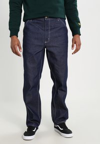 Dark blue denim jeans with a relaxed fit, contrasting light stitching, a front button closure, and two side pockets. Worn with black sneakers.