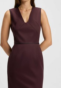 Bordeauxfarvet ærmeløs kjole med V-udskæring, der har geometriske sømdetaljer og en figursyet silhuet, lavet af glat, struktureret stof.