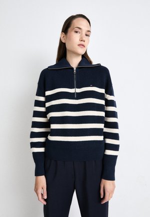 Maglione a strisce navy e crema in maglia con colletto zip. Presenta una texture a coste e un piccolo logo sul petto.