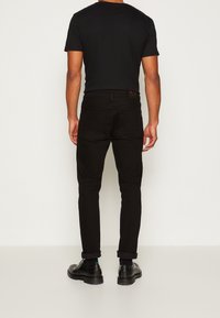 Černé slim-fit džíny s čistým designem, vyrobené z denimu. Mají ohrnuté nohavice a zadní kapsu s označením značky.