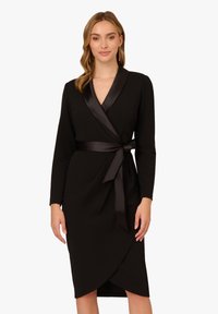 Schwarzes Wickelkleid mit langen Ärmeln, Satinakzenten und einem Bindegürtel. Es hat einen V-Ausschnitt und einen asymmetrischen Saum für eine strukturierte Silhouette.