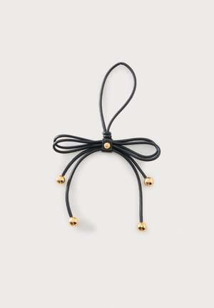 Black leather bow with a loop and four hanging ends, each ending with a small round gold bead against a plain light background.