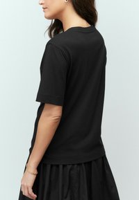 Zwarte katoenen T-shirt met korte mouwen, ronde hals en een relaxte pasvorm, gedragen met een vloeiende zwarte rok die een gladde textuur laat zien.