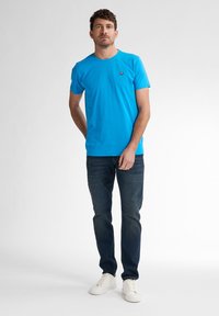 Modré bavlněné tričko s kulatým výstřihem a malou nášivkou. V kombinaci s tmavě modrými džíny a bílými teniskami. Jednoduchý a nezdobený design.