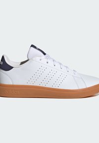 Zapatilla blanca de cuero con diseño perforado en el lateral, puntera redonda y suela de goma marrón. Presenta cordones blancos y una lengüeta en el talón de color marino.