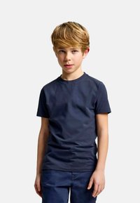 T-shirt di cotone blu navy con maniche corte e collo rotondo, indossato da un bambino in piedi contro uno sfondo bianco uniforme.