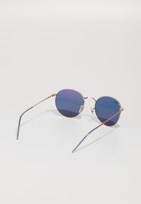 Ochelari de soare rotunzi cu ramă din metal roz aurie, lentile de culoare albastră închisă și tije subțiri și curbe. Pads pentru nas ajustabile pentru confort.