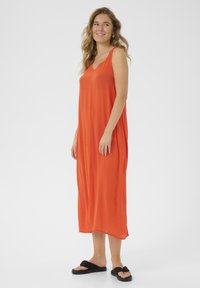 Orange, ärmlös maxiklänning med V-ringning, flödande silhuett, tillverkad av lättviktig tyg. Kombinerad med svarta, platta sandaler.