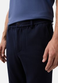 Marineblauwe joggingsbroeken met een elastische tailleband, een knoopsluiting en zijzakken. De stof lijkt zacht en gestructureerd.