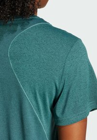 Teal urheilupaita, jossa on sileä, heather-kangas. Tässä on lyhyet hihat ja kaareva sauma yksityiskohtana selkävartalon alueella.