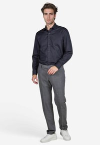 Donkerblauw overhemd met lange mouwen en knopen aan de voorkant, gecombineerd met grijze geruite broek en witte sneakers; gladde stof en pasvorm op maat.