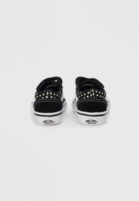 Baskets en suède noir avec des semelles blanches, présentant un motif à pois à l'arrière et des coutures blanches contrastantes. Marque sur le talon.
