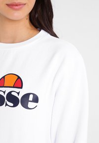 Sudadera blanca con cuello redondo que presenta un gran logotipo colorido en azul marino, naranja y amarillo. Tejido suave con un corte casual.
