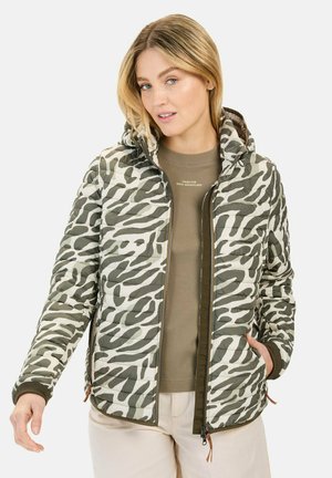 Quilted Jacke in einem grün-beigen Zebramuster. Verfügt über eine Kapuze, einen Reißverschluss und elastische Bündchen. Getragen über einem beigen Hemd und hellen Hosen.