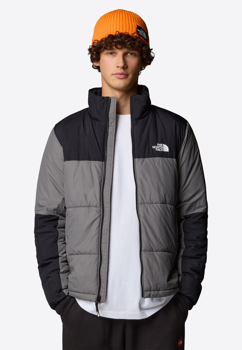 Gevoerde jack in grijs en zwart met een hoge kraag en ritsluiting. Gemaakt over een wit shirt, met het North Face-logo op de borst.
