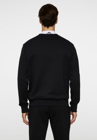 Felpa nera con maniche lunghe, scollatura tonda e polsini a costine. Realizzata in tessuto liscio, presenta un logo sul colletto posteriore.