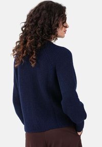Pull en maille bleu marine avec une texture côtelée, coupe décontractée et manches longues légèrement bouffantes. Il présente un col rond et des coutures d'épaule tombantes.