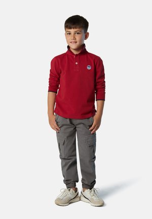 Polo rojo de manga larga con cuello y logo, combinado con pantalones cargo grises que tienen bolsillos y puños elásticos, llevados con zapatillas blancas.