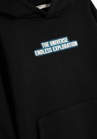 Svart hoodtr�öja med en framficka, med vit och blå broderad text: "UNIVERSET ENDAST UTFORSKNING." Mjuk textur, avslappnad design.