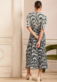 Svart och vit blommig klänning med korta ärmar, röd kant och midja som är draperad, tillsammans med beige blockklacksandaler.